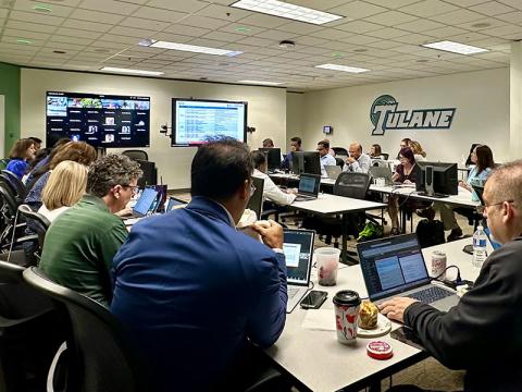 People work on laptops in a Tulane classroom with wall monitors showing data.