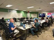 People in a green-walled conference room, working on laptops with screens displaying content.