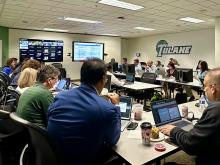 People work on laptops in a Tulane classroom with wall monitors showing data.