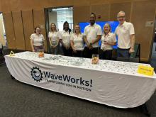 Group photo of 7 people standing by WaveWorks table